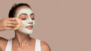 A person holds a skincare sponge to their cheek, showcasing a natural beauty routine against a soft pink background.