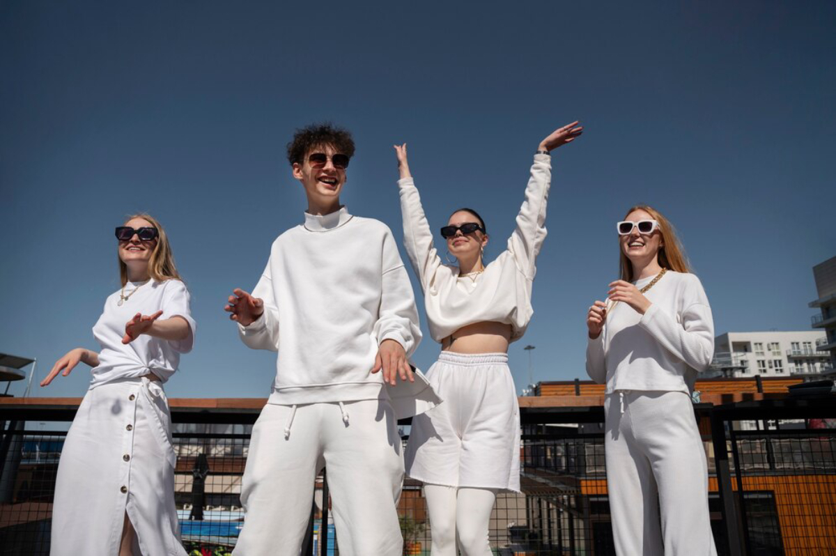 A group of four people poses against a clear blue sky, all dressed in stylish white outfits.