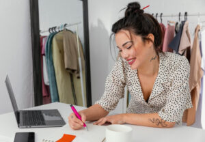 A person in a polka dot blouse takes notes with a pink pen at a desk.