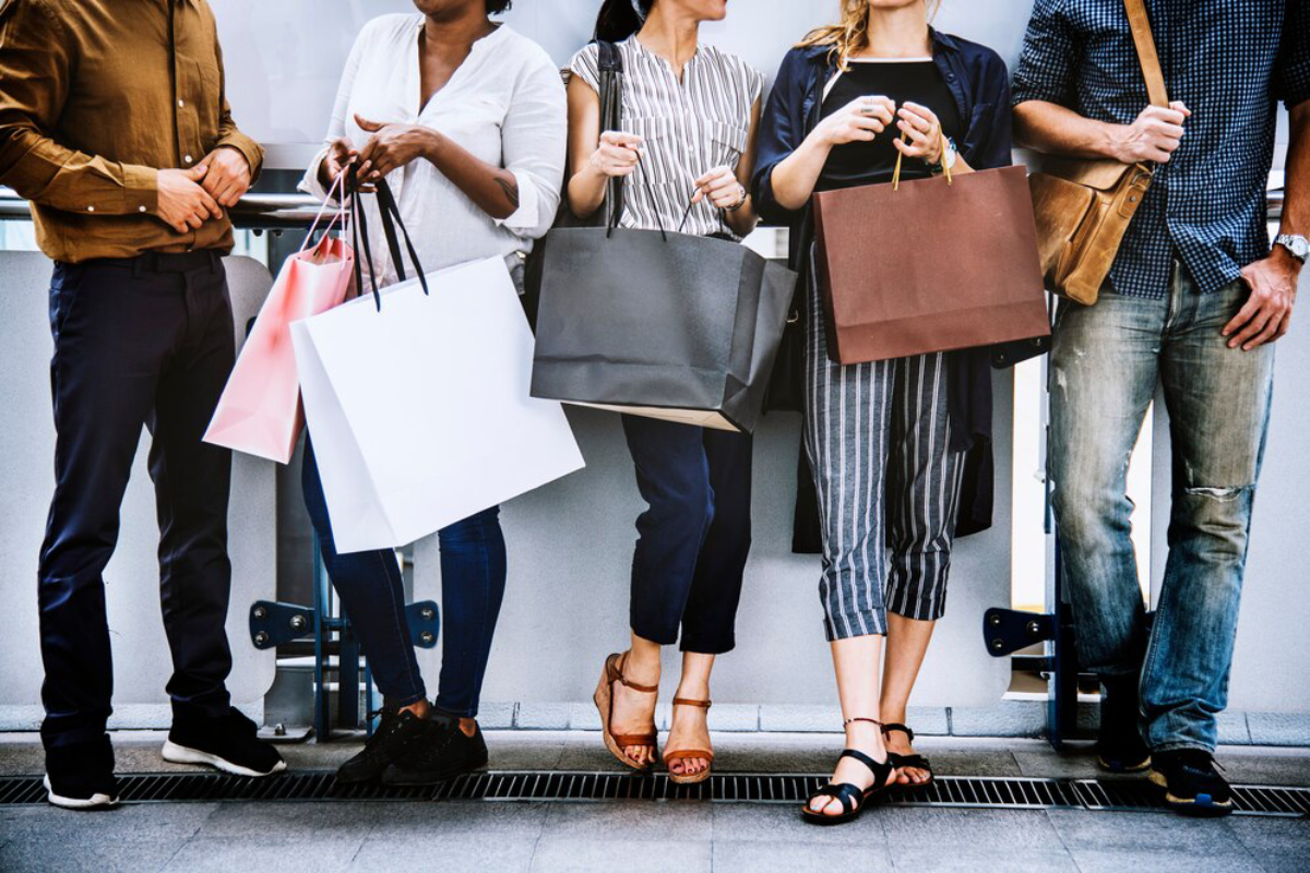 A diverse group of shoppers stand together holding various shopping bags.