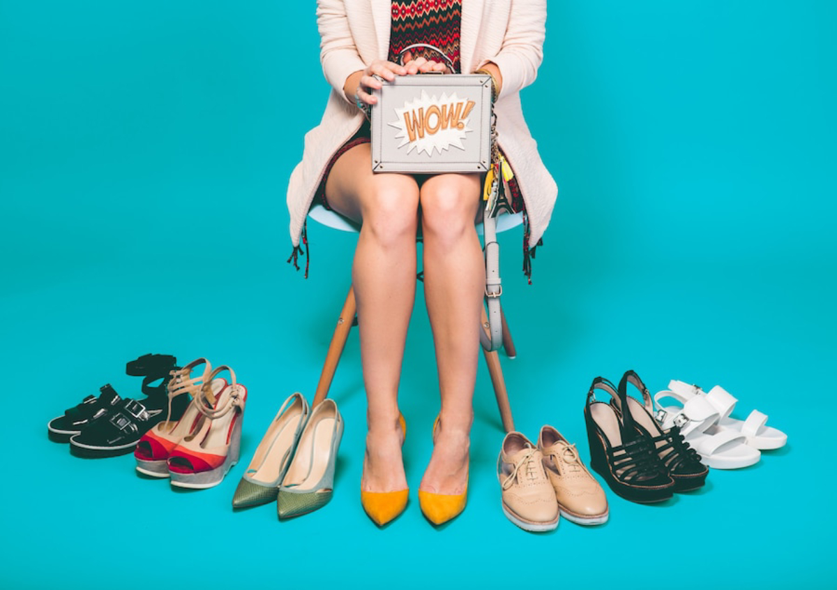 A woman sits on a chair with various stylish shoes arranged on both sides.
