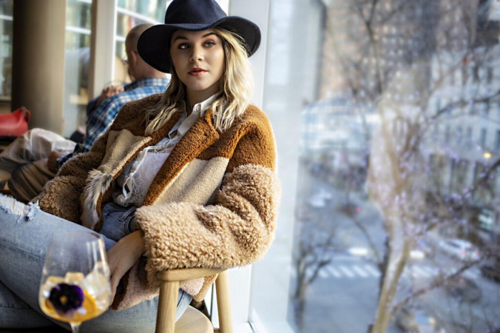 A person in a cozy, multi-toned fleece jacket sits comfortably by a large window.