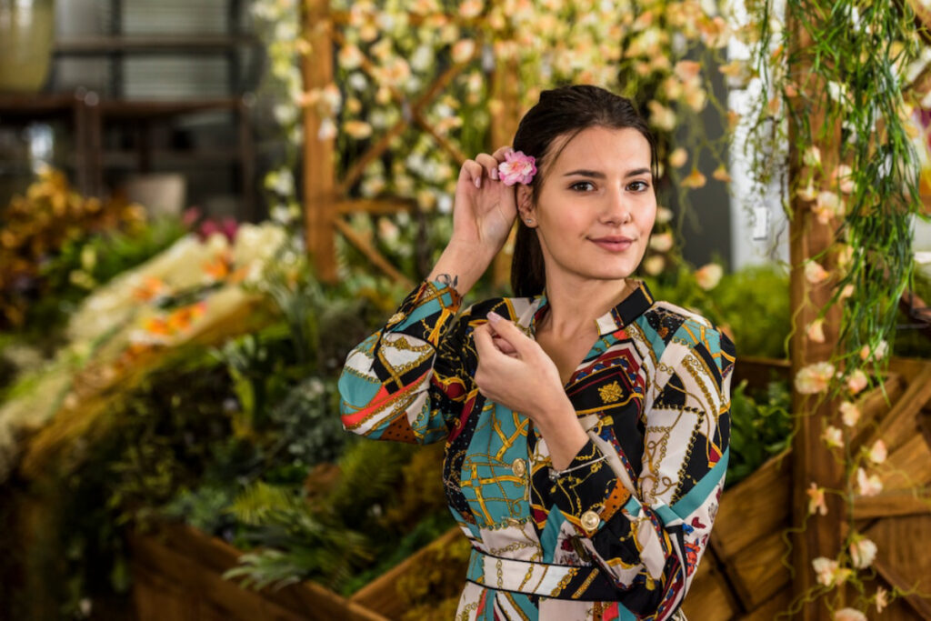 A woman in a colorful patterned blouse places a small pink flower behind her ear.