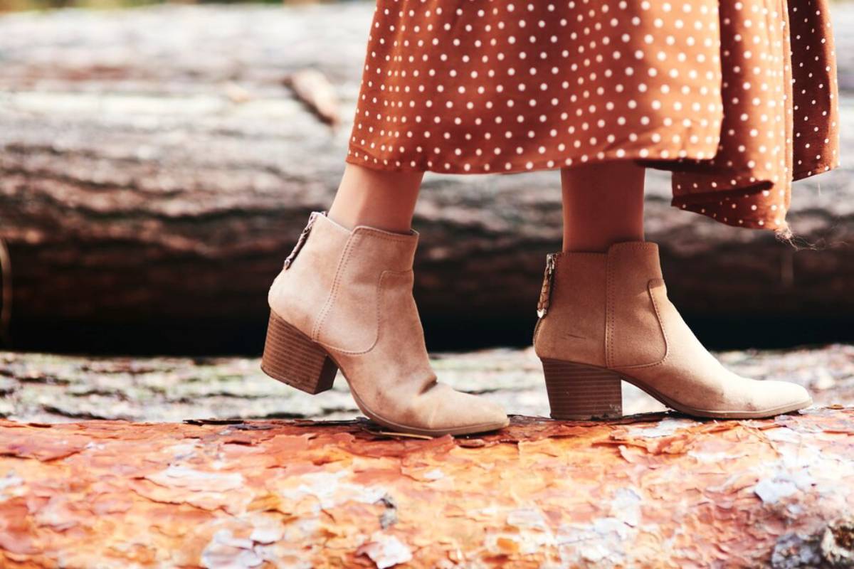 A pair of stylish beige ankle boots on a woman walking along a log