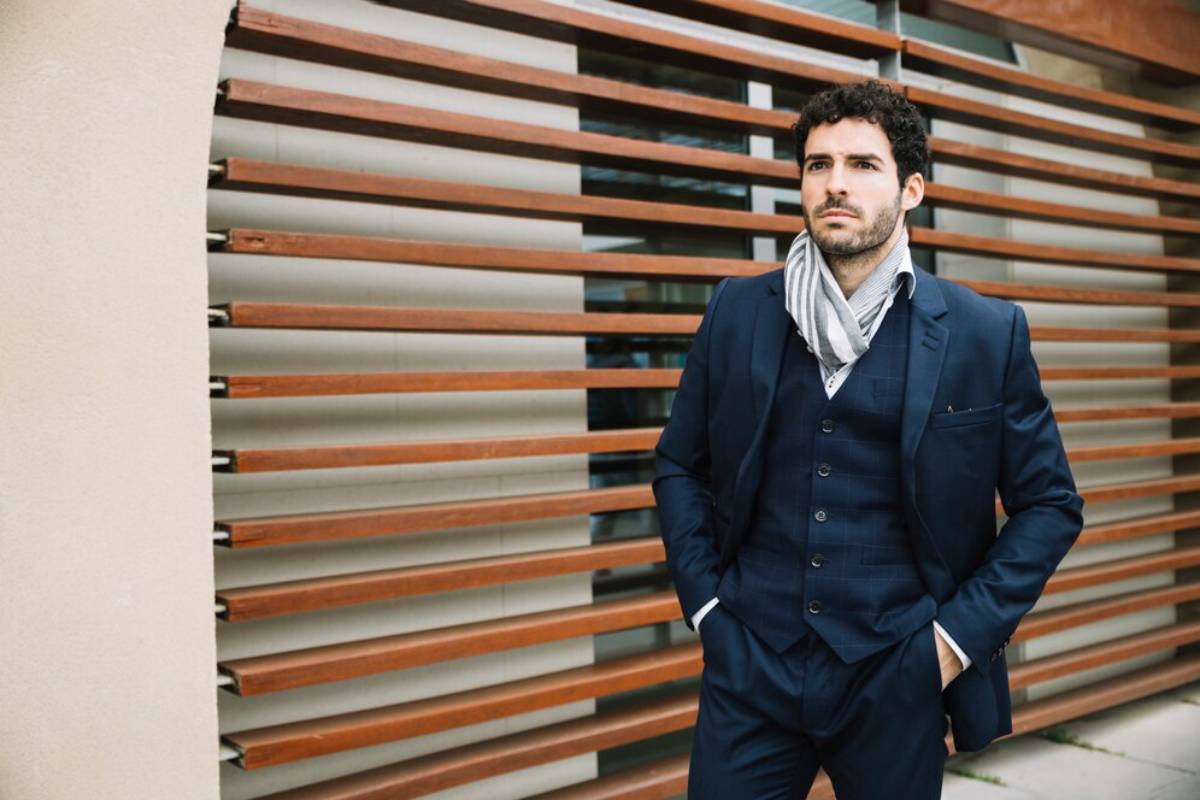 A man in a navy suit and striped scarf poses confidently
