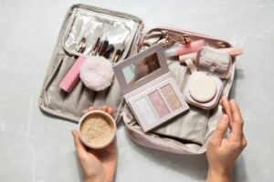 Flat lay of beauty products and accessories on a vibrant yellow background, featuring a notebook, makeup brushes, perfume, and jewelry.